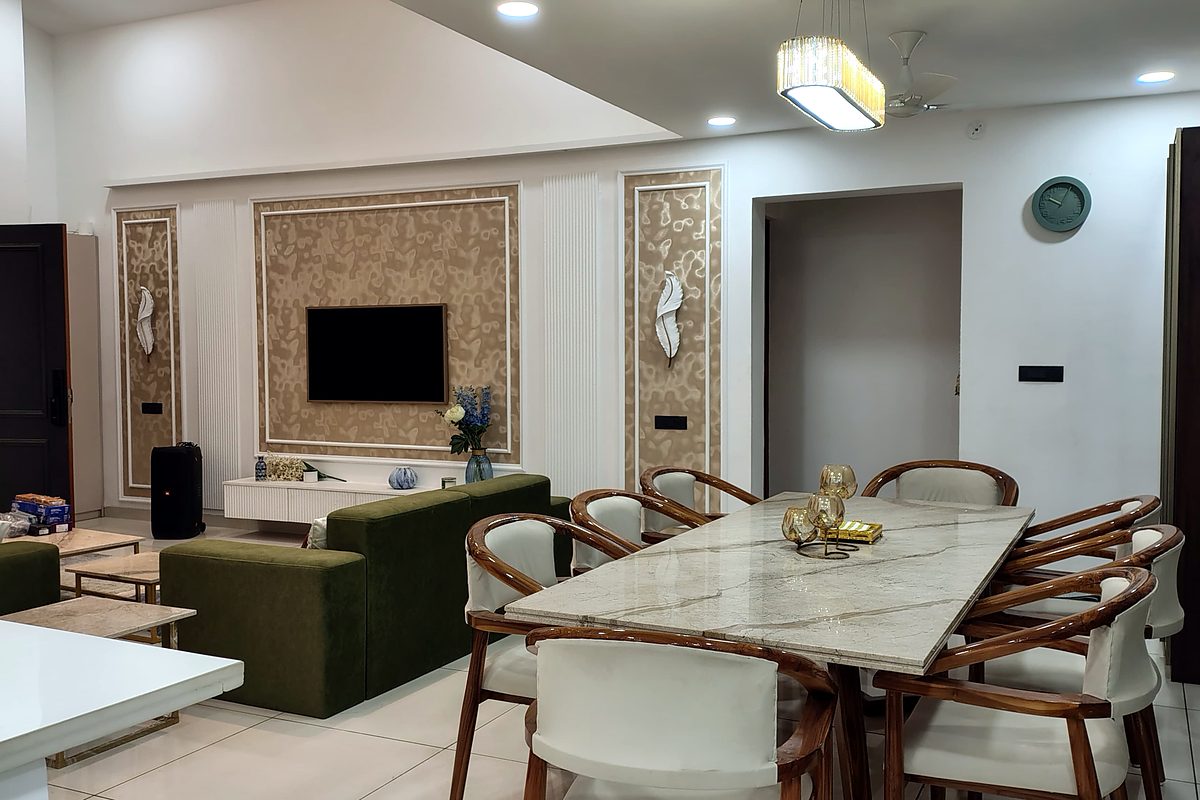 Completed living and dining interior with an olive velvet sofa, panelled television wall, marble dining table and a gold pendant over the table